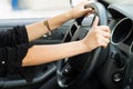 Closeup inside vehicle of hands holding onto steering wheel, black interior background, female driver concept