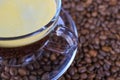 Closeup of isoalted transparent glass cup, saucer and handle with black coffee whitecap crema, blurred roasted coffee beans Royalty Free Stock Photo