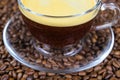 Closeup of isoalted transparent glass cup, saucer and handle with black coffee whitecap crema, blurred roasted coffee beans Royalty Free Stock Photo