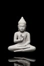 Buddha statue seated in light grey stone with black background making a sign with his left hand and in levitation