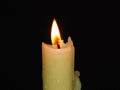 Closeup of an isolated burning candle on dark black background. Flame, light, candle wax. Mystery, religion concept. 