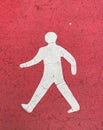 Closeup of isolated white pedestrian sign painted on red cracked rough asphalt ground Royalty Free Stock Photo