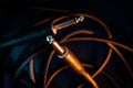 Closeup of Jack Connectors on Quarter Inch Cord in Front of Tangled Wire on Teal Backdrop with Orange Lighting