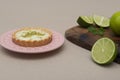 Closeup of a key lime tartlet on a pink plate with some sliced key limes on a wooden board
