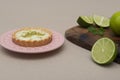 Closeup of a key lime tartlet on a plate with some sliced key limes on a wooden board