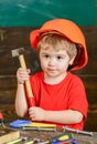 Closeup kid in orange helmet holding hammer in his hands. Crafts lesson at kindergarten. Portrait of little boy in Royalty Free Stock Photo