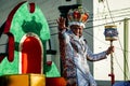 Closeup king of carnival riding on open platform waves to people on city street