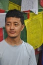 Closeup of a Ladakhi young guy looking sideways, standing against Buddhist prayer flags