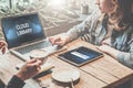 Closeup of laptop with inscription on monitor - cloud library on table at which sit two women. On table digital tablet, notebook Royalty Free Stock Photo