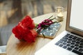 Closeup laptop screen and keyboard on wooden table. Roses red flowers present for St. Valentine`s Day.