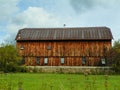 Closeup of large antique cedar wood barn with stone foundation centered in green field.