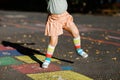 Closeup of leggs of little toddler girl playing hopscotch game drawn with colorful chalks on asphalt. Little active