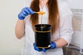 Closeup liquid sugar on a stick flows into a black jar in the hands of a depilation master.