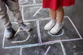 Closeup of little boy`s and girl`s legs and hopscotch drawn on asphalt. Child playing hopscotch game on playground outdoors on a Royalty Free Stock Photo