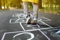 Closeup of little boy`s legs and hopscotch drawn on asphalt. Child playing hopscotch game on playground outdoors on a sunny day