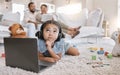 Closeup of a little cute girl using a laptop and wireless headphones while laying on the floor in the lounge. Hispanic Royalty Free Stock Photo