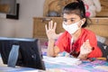 Closeup of Little girl kid student wearing mask raise her hand while studying online class with tablet at home, New normal.Covid- Royalty Free Stock Photo