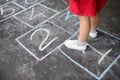 Closeup of little girl`s legs and hopscotch drawn on asphalt. Child playing hopscotch game on playground outdoors on a sunny day