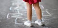 Closeup of little girl`s legs and hopscotch drawn on asphalt. Child playing hopscotch game on playground outdoors on a sunny day