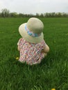 Closeup of little girl sitting in grass at a park wearing a straw hat and looking off into distance Royalty Free Stock Photo