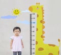 Closeup little girl stand for measure height with cute giraffe cartoon at the marble stone wall textured background Royalty Free Stock Photo