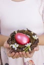 Closeup little girls hands holding pink Easter egg in the nest.