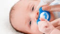 Closeup of little newborn baby lying in crib while mother cleaning his nose with nasal aspirator and taking out mucus