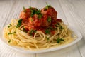 Closeup of a lone plate with cooked spaghetti with meatballs seasoned with parsley, on a white wooden table Royalty Free Stock Photo