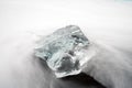 Closeup and long exposure shot of clear ice chunk on black lava beach in Iceland.