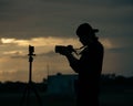 Closeup of a long hair photographer filming on a tripod at sunset