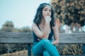 Closeup of a lovely young girl sitting on a wooden bench with her hand on her chin in a park Royalty Free Stock Photo