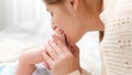 Closeup of loving and caring mother holding and kissing little feet of her newborn baby boy on bed. Concept of family Royalty Free Stock Photo