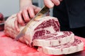 Closeup macro cook`s hand cut ribeye marbled beef steak with knife on red plastic cutting board on metal table in restaurant Royalty Free Stock Photo