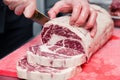 Closeup macro cook`s hand cut ribeye marbled beef steak with knife on red plastic cutting board on metal table in restaurant