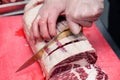 Closeup macro cook`s hand cut ribeye marbled beef steak with knife on red plastic cutting board on metal table in restaurant