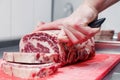 Closeup macro cook`s hand cut ribeye marbled beef steak with knife on red plastic cutting board on metal table in restaurant