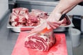 Closeup macro cook`s hand cut ribeye marbled beef steak with knife on red plastic cutting board on metal table in restaurant