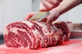 Closeup macro cook`s hand cut ribeye marbled beef steak with knife on red plastic cutting board on metal table in restaurant