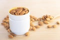 Closeup or macro of organic raw peeled almond nuts in cup and spoon with almonds laid around cup on wooden background