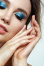 Closeup macro shot of human female face with hands near face, yellow liner and blue eyes shadows makeup