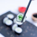 Closeup of Maki roll held with black chopsticks. Fresh hosomaki pieces with rice and nori. Close Up of delicious japanese food Royalty Free Stock Photo