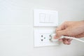 Closeup Male finger unplugging or plugging of electricity device on white wall at home. Energy Saving, power, electrical and