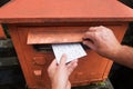 Closeup on a male hand putting a letter in a red letterbox. Concept of vintage type of communication.