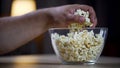 Closeup of male hand taking popcorn from bowl on table, unhealthy food addict