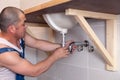 Closeup male plumber worker in blue denim uniform, overalls, fixing sink in bathroom with tile wall. Professional Royalty Free Stock Photo