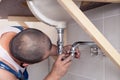 Closeup male plumber worker in blue denim uniform, overalls, fixing sink in bathroom with tile wall. Professional plumbing repair Royalty Free Stock Photo