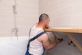 Closeup male plumber worker in blue denim uniform, overalls, fixing sink in bathroom with tile wall. Professional plumbing repair Royalty Free Stock Photo