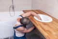 Closeup male plumber worker in blue denim uniform, overalls, fixing sink in bathroom with tile wall. Professional plumbing repair Royalty Free Stock Photo