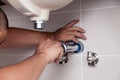 Closeup male plumber worker in blue denim uniform, overalls, fixing sink in bathroom with tile wall. Professional plumbing repair