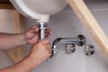 Closeup male plumber worker in blue denim uniform, overalls, fixing sink in bathroom with tile wall. Professional plumbing repair Royalty Free Stock Photo